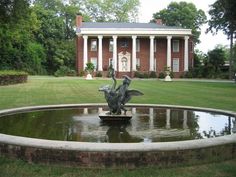 a fountain in front of a large brick building with columns on the side and a statue of a bird sitting on top of it