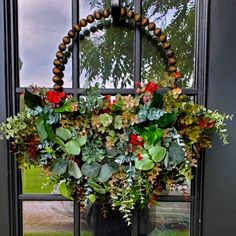 a wreath hanging on the side of a door decorated with greenery and red flowers