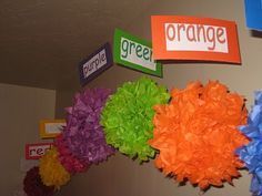 colorful paper flowers are hanging on the wall in front of orange and green signs with name tags