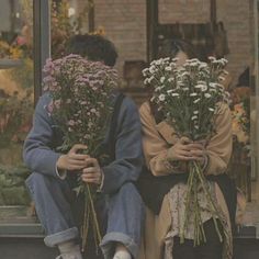 two people sitting on the ground holding flowers