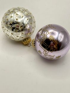 two shiny glass ornaments on a white surface