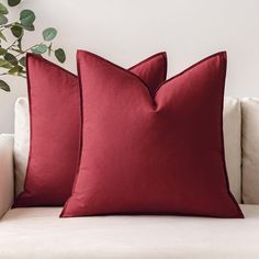 two red pillows sitting on top of a white couch next to a potted plant