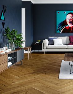 a living room with blue walls and wood flooring is pictured in this image, the painting on the wall shows a man's face