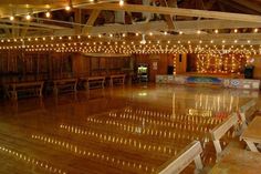 an empty dance floor with lights strung from the ceiling and wooden benches to the side