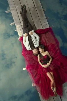 a man and woman laying on top of a wooden pier next to eachother