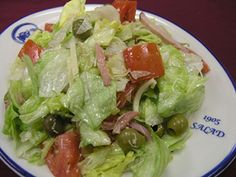 a salad with lettuce, tomatoes and olives on a white and blue plate