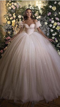 a woman in a ball gown posing for the camera with flowers around her and an archway behind her