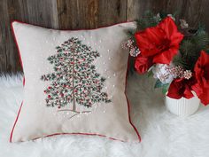 a christmas tree pillow sitting next to a vase with poinsettis