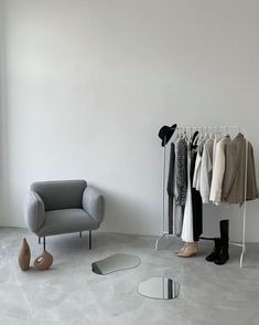 an empty room with clothes on hangers and a chair next to it, in front of a mirror