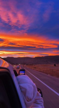 the sun is setting over an open highway with cars driving on it and mountains in the distance