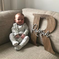 a baby sitting on top of a couch next to a wooden letter that says roman