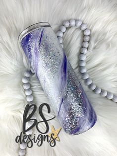 a purple and silver tumbler sitting on top of a white fur covered floor next to a beaded necklace