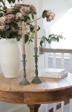 two candles are sitting on a table with flowers in a vase and some books next to it