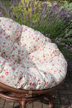 a round chair cushion sitting on top of a wooden stool in front of purple flowers