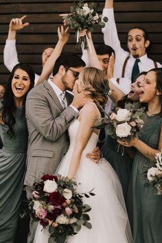 a group of people standing next to each other holding bouquets in the air with their hands up