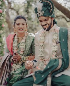 a man and woman sitting next to each other in front of trees with garlands on their heads