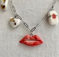 Vintage-themed charm necklace on a gold bar chain; all the charms are sculpted from a fine white porcelain clay and painted by hand to have charming details. Back and front sides are painted. Since they are made from porcelain and glossed with a clear glaze, each charm is smooth and soft to the touch.  Each charm is attached to a small, gold jump ring that can be attached to a necklace chain. Small charms featured: Blue-green Sea Star, Love Letter w/ gold highlights, Red Lipstick with gold band, Red lips, Slipper with gold heart, Gold Heart (gold raindrops on one side, gold heart on the other), Lucky Strikes pack. Bought individually, your charm(s) will come with a thin, black velvet ribbon to tie as a choker necklace. You can also buy a 7-charm necklace that comes with a gold bar necklace Gold Highlights, Gold Bar Necklace, Small Charms, Hand Painted Porcelain, Velvet Ribbon, Bar Necklace, Gold Bands, Chains Necklace, Charm Necklace