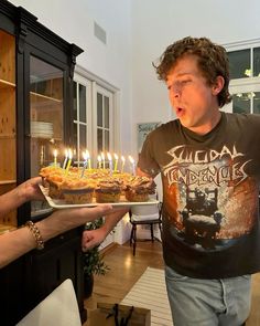 a young man holding a tray full of cupcakes with lit candles on them