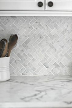 a white kitchen with marble backsplash and stainless steel oven mitts on the counter