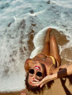 a woman laying on top of a sandy beach next to the ocean