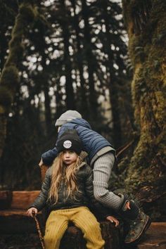 two people are sitting on a bench in the woods, one is holding his head over the other's shoulder