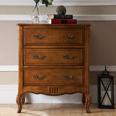 a wooden dresser sitting next to a lamp and vase with flowers on top of it