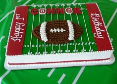 a football themed cake on top of a green tablecloth covered field with white and red icing