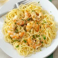 pasta with shrimp and parmesan cheese on a white plate next to a glass of wine