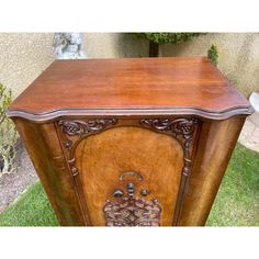 an old fashioned wooden cabinet with carvings on the front and sides, sitting in grass