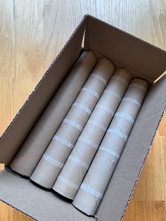 an open cardboard box filled with rolls of toilet paper on top of a wooden floor