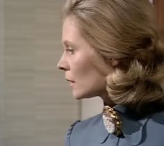 a woman in a blue dress with a gold brooch on her left shoulder and hair pulled back to the side