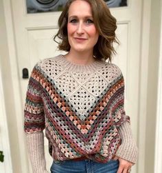 a woman standing in front of a door wearing a crocheted sweater and jeans