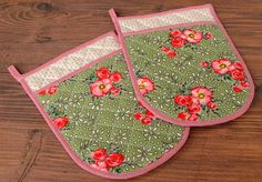 two oven mitts with red flowers on them sitting on a wooden table next to each other