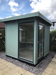 a small green shed sitting in the middle of a gravel area next to a fence