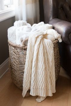 a chair with a blanket and blankets on it next to a leather chair in front of a window