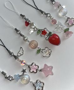 several necklaces with charms on them sitting on a white plate, one has a strawberry and the other is a star