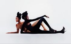 two women in black bodysuits sitting on the floor with their arms around each other