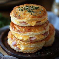 stack of pancakes topped with ham and cheese on a black plate next to green leaves