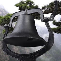 a bell hanging from the side of a tree with mountains in the backgroud