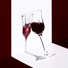 two glasses of red wine are sitting on a white counter top, one is half filled and the other half empty