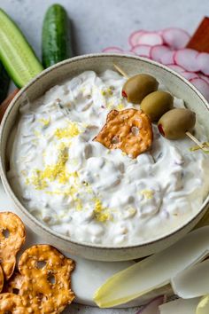 a bowl of dip surrounded by crackers, pretzels and celery