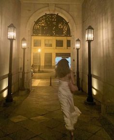 a woman in white dress walking down a hallway with lights on either side of her