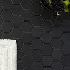 a white towel sitting on top of a black tiled floor next to a potted plant