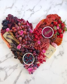 a heart - shaped arrangement of fruits and cheeses on a marble countertop with pink flowers