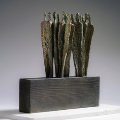 three metal sculptures sitting on top of a wooden block in front of a white wall