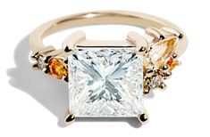 an engagement ring with three different colored stones on it's sides and a princess cut diamond in the center