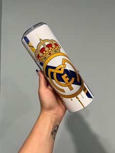 a hand holding up a can with the emblem of real madrid on it's side