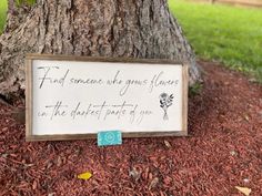 a sign on the ground under a tree that says, find someone who gives flowers in the darkest parts of you