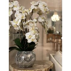 a glass vase with white flowers sitting on top of a wooden table next to a couch