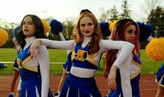 three girls in cheerleader outfits standing on a field